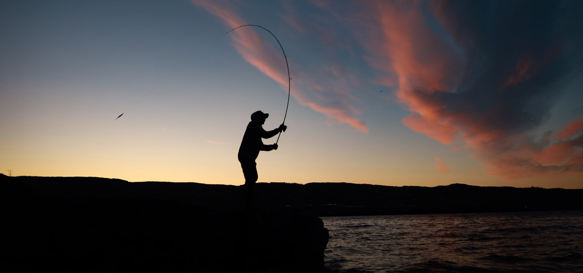Fisker ved sjøen i solnedgang – perfekt øyeblikk for kveldens storfangst.